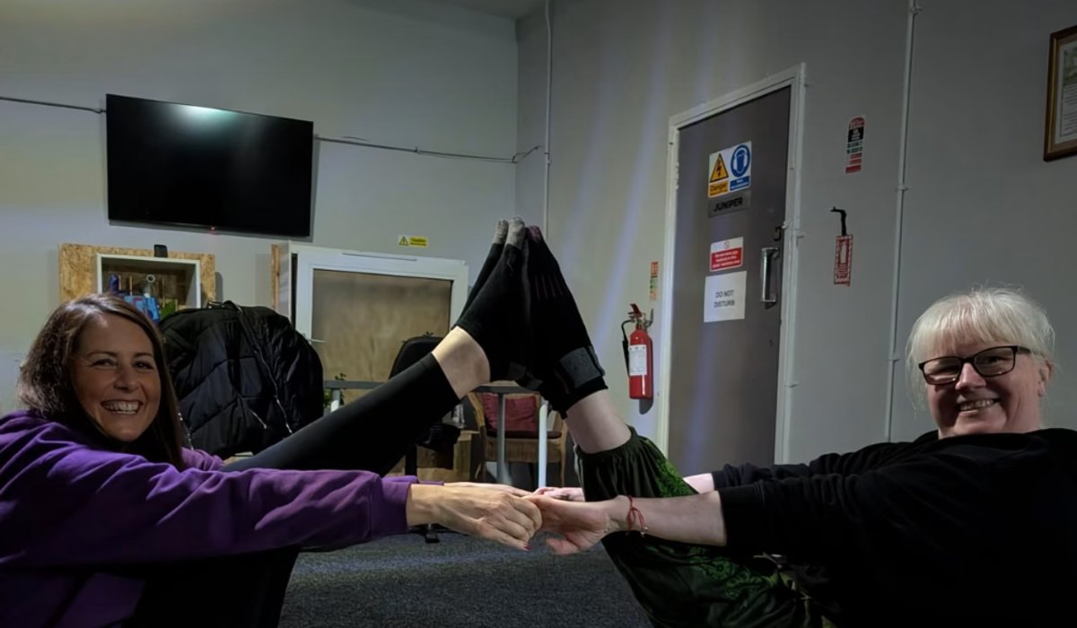 Stephanie sharing a laugh with a client mid partner-yoga pose in the studio